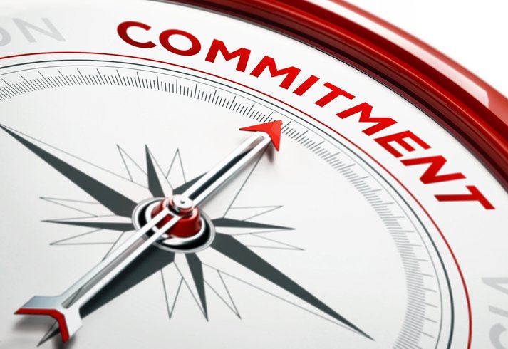 Arrow of a compass is pointing commitment text on the compass. Arrow , commitment text and the frame of compass are metallic red in color. White background. Horizontal composition with copy space. Commitment concept.